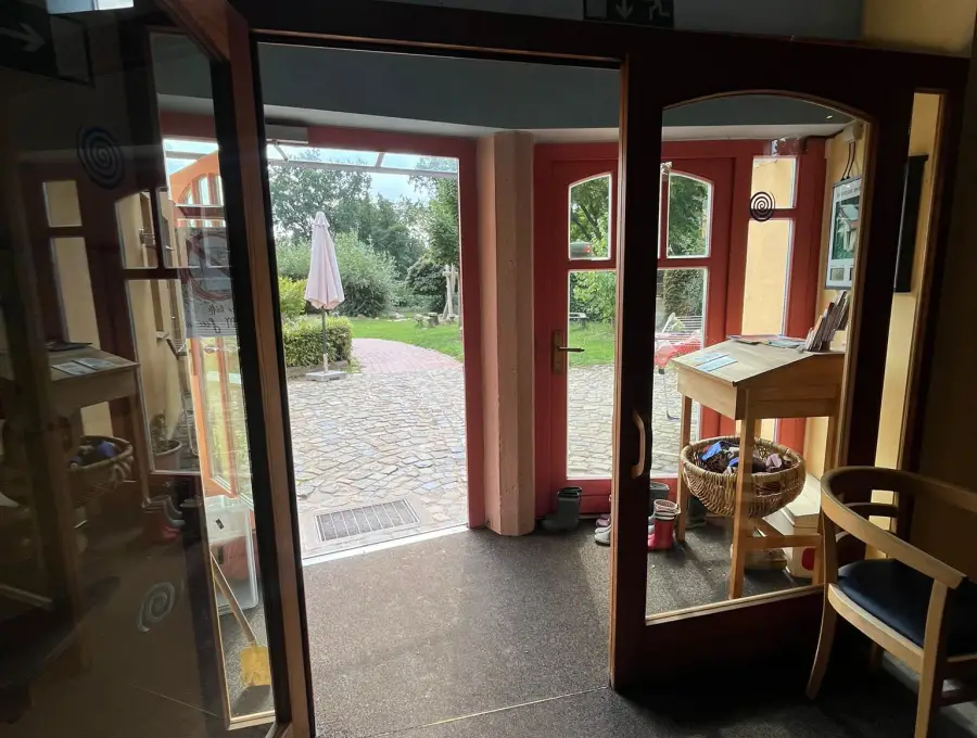 Der Eingangsbereich mit weit geöffneten Glastüren, ebenerdigem Übergang und Blick auf den gepflasterten Hof