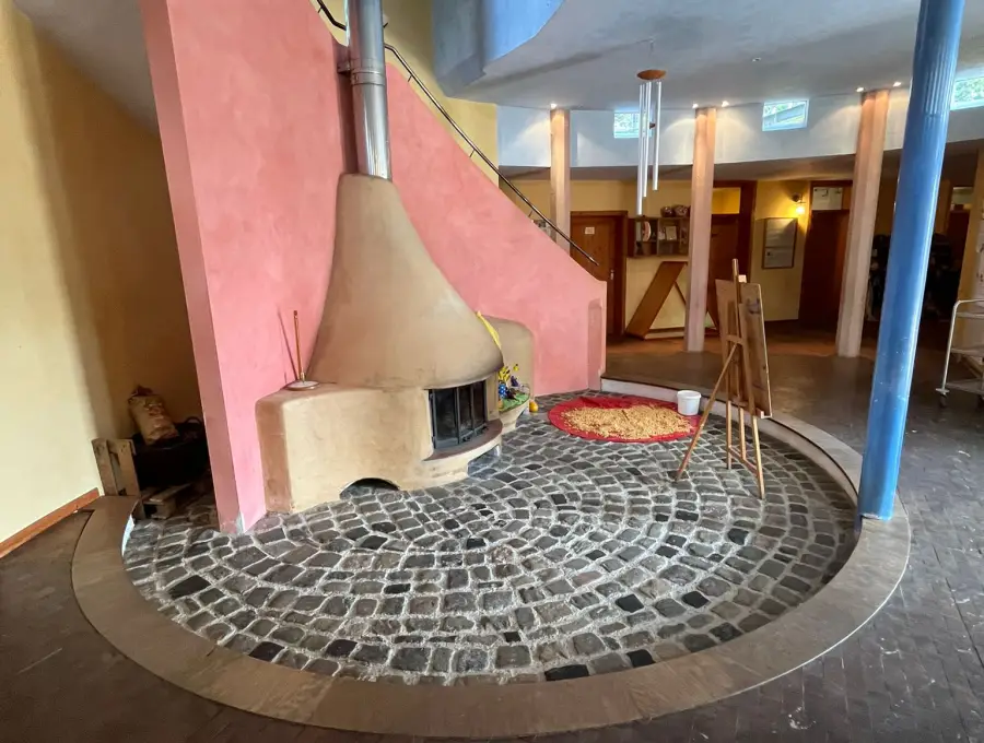 Das Foyer mit dem runden Lehmofen auf einem Kopfsteinpflaster-Rund, daneben eine blaue Säule