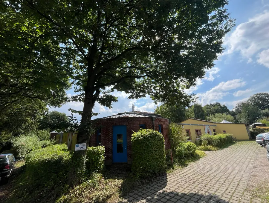Die Zufahrt zum Kinderhaus, links der Backsteinturm mit blauer Tür unter einem großen Kastanienbaum