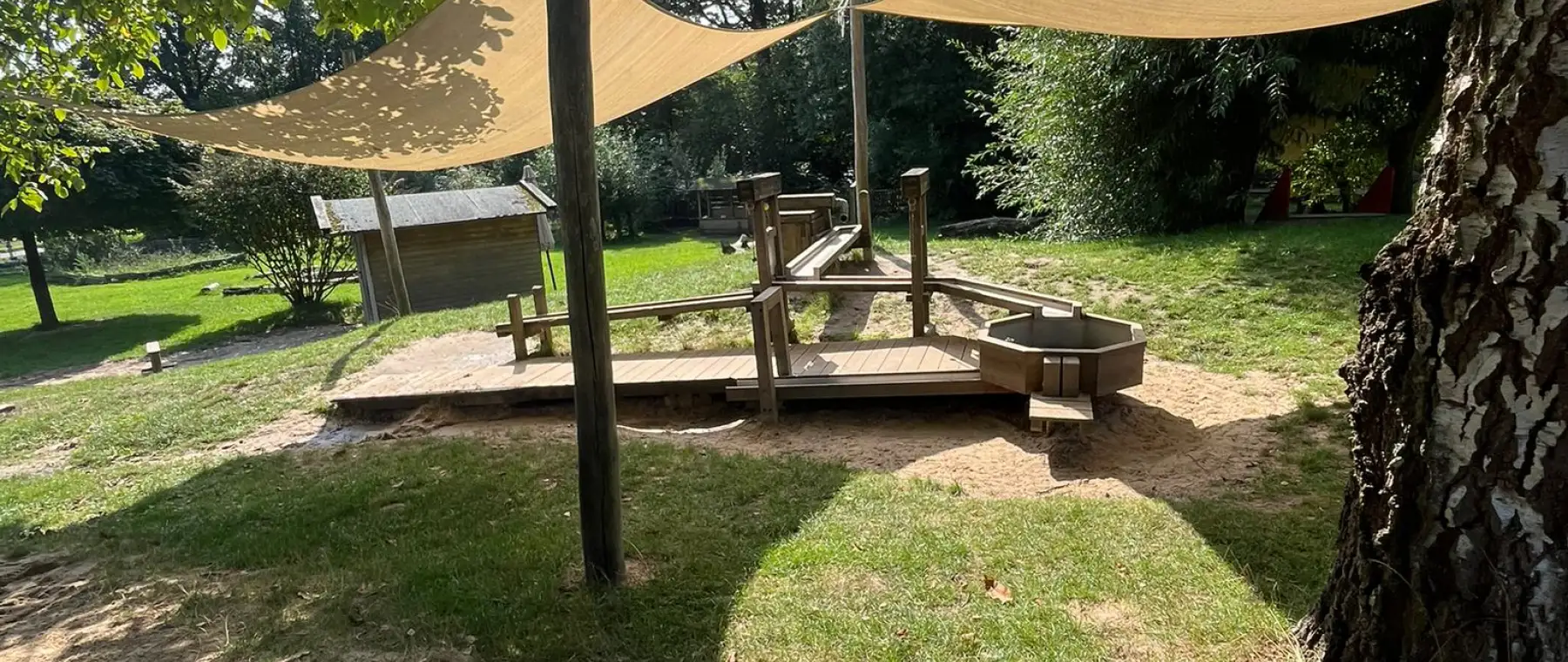 Der Sandkasten unter dem Sonnensegel, dahinter die Holzterrasse