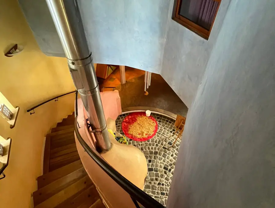 Blick von oben über eine geschwungene Holztreppe in das Foyer mit Kopfsteinpflaster und rundem rotem Teppich