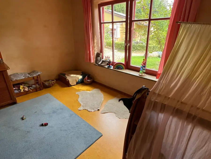 Ein ruhiger Raum mit weichem Teppich, Fellen auf dem Boden und einem Bett mit hellem Betthimmel am Fenster
